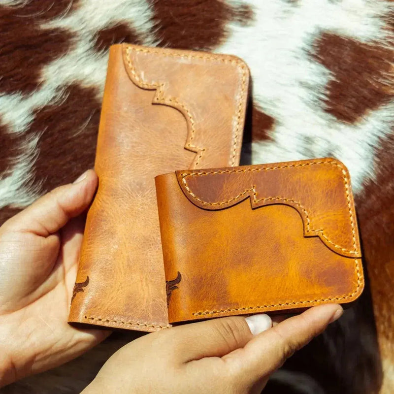 One long leather wallet and one bifold leather wallet, both handmade in Texas in the color saddle tan, with carefully detailed stitching.
