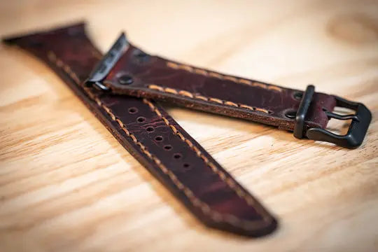 Dark brown handmade leather apple watch band with contrast stitching and black hardware, displayed on a light wood surface.