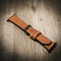 Apple Watch Leather Band in tan full-grain leather with contrast stitching and black hardware on a wooden surface.
