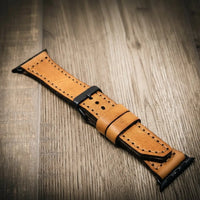 Premium tan full-grain leather Apple Watch band with black buckle on wood surface.