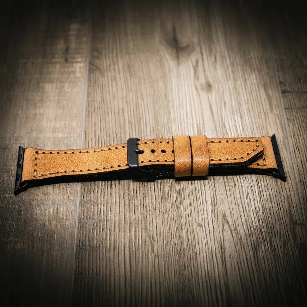 Light tan full-grain leather Apple Watch band with black buckle and stitched edges on wood surface.