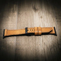 Light tan full-grain leather Apple Watch band with black buckle and stitched edges on wood surface.